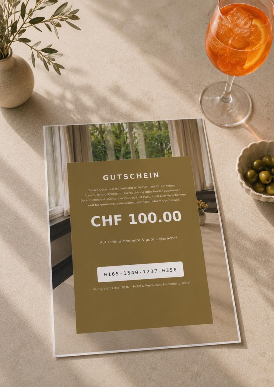 Eine 100-Franken-Gutscheinkarte für das Hotel & Restaurant Bärenberg Lenzau liegt auf einem Tisch neben einem Apéro: ein Glas Orangengetränk, grüne Oliven und eine Vase mit Olivenzweigen. Das Sonnenlicht fällt durch das Fenster.