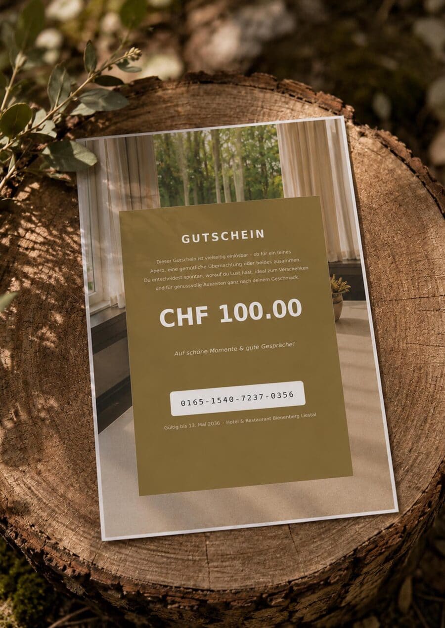 Ein 100 CHF Gutschein ruht auf einem Baumstumpf im Freien, umgeben von Blättern. Der Gutschein hat einen deutschen Text, einen einzigartigen Code und ist mit einem eleganten, modernen Design in Erdtönen bedruckt.